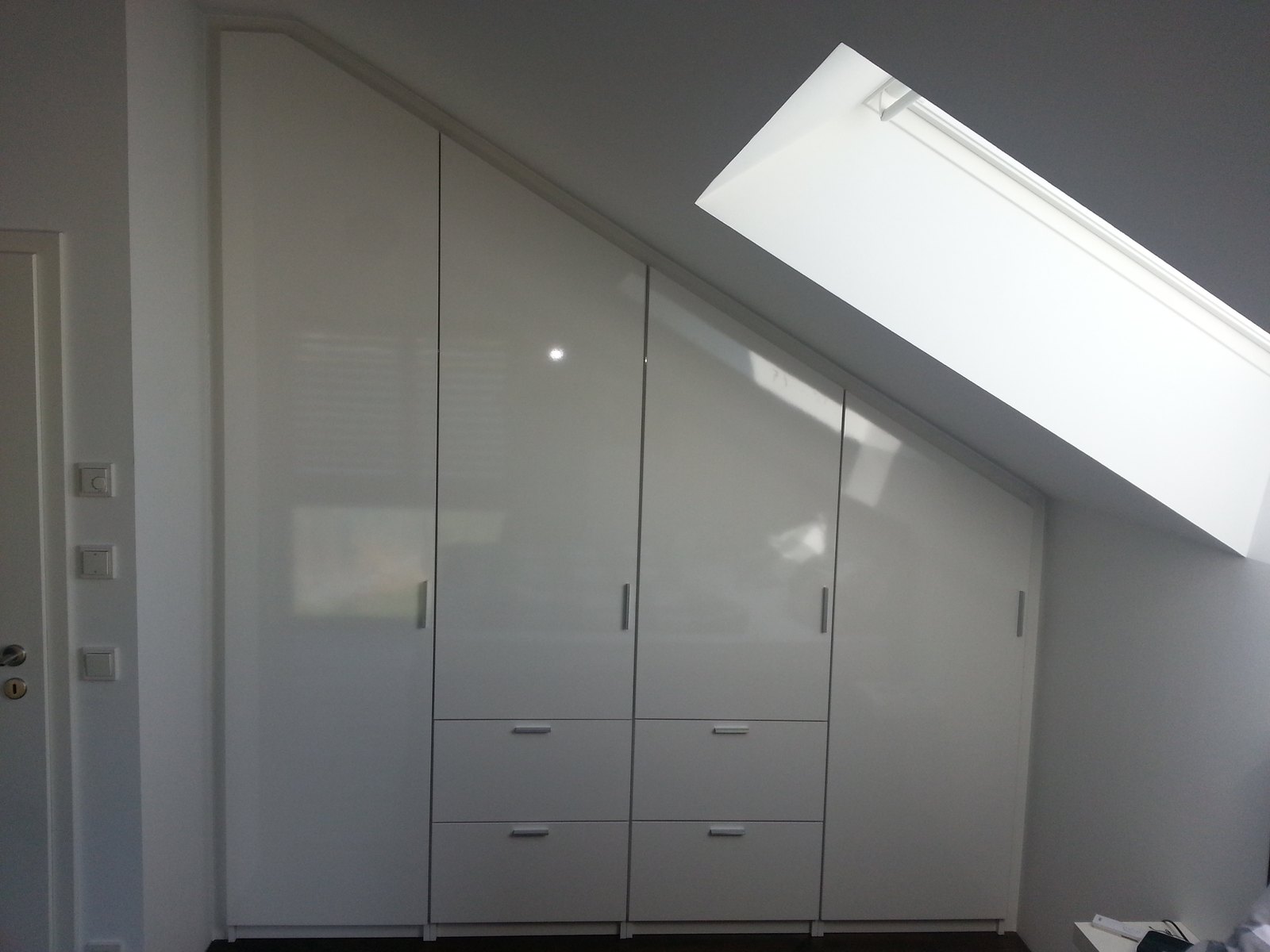 Einbauschrank mit weißen Türen und Schubladen unter einer Dachschräge, daneben ein Dachfenster