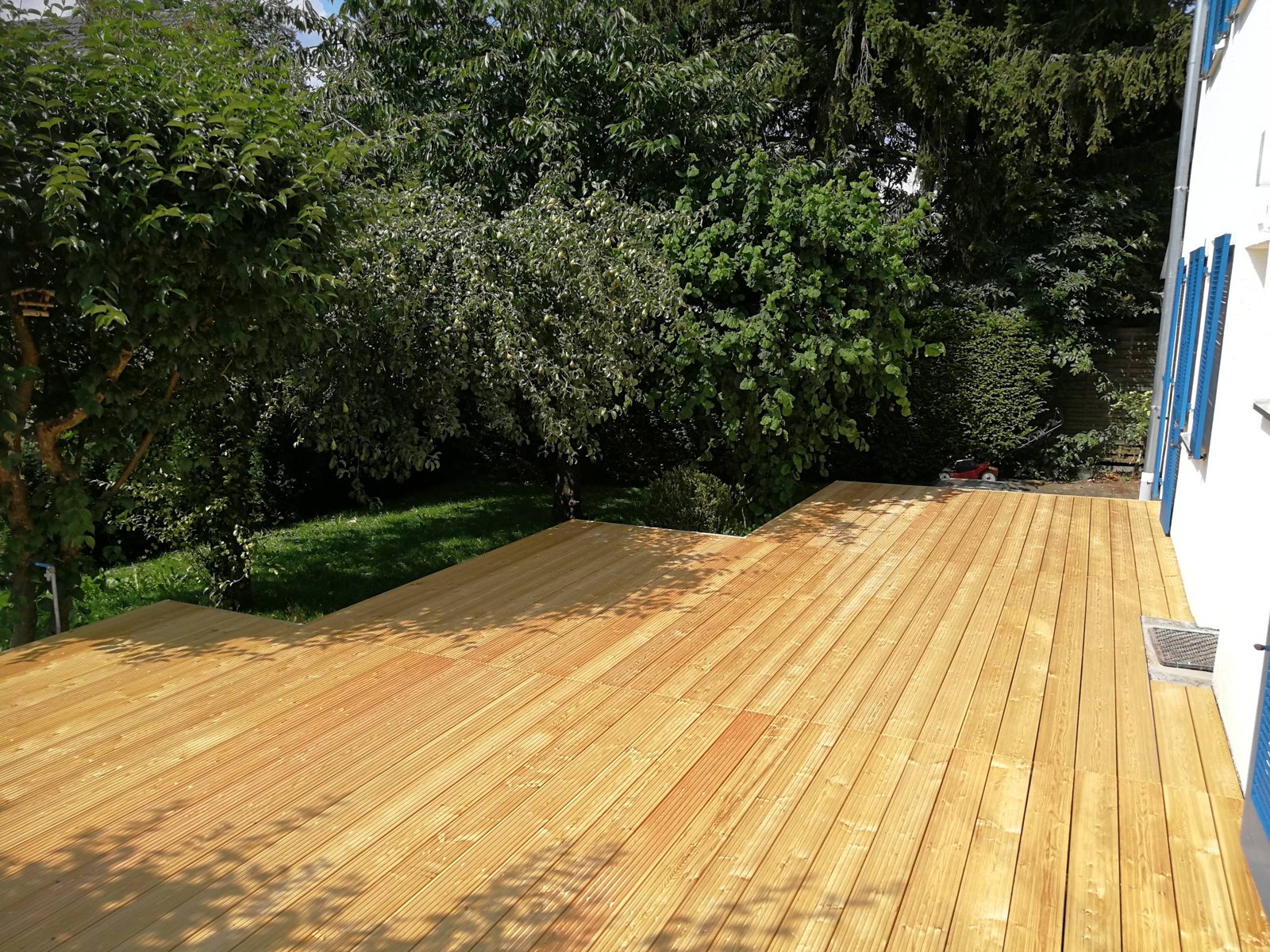 Terrasse mit Holzdielen an einem Haus, dahinter ein Garten mit Obstbäumen